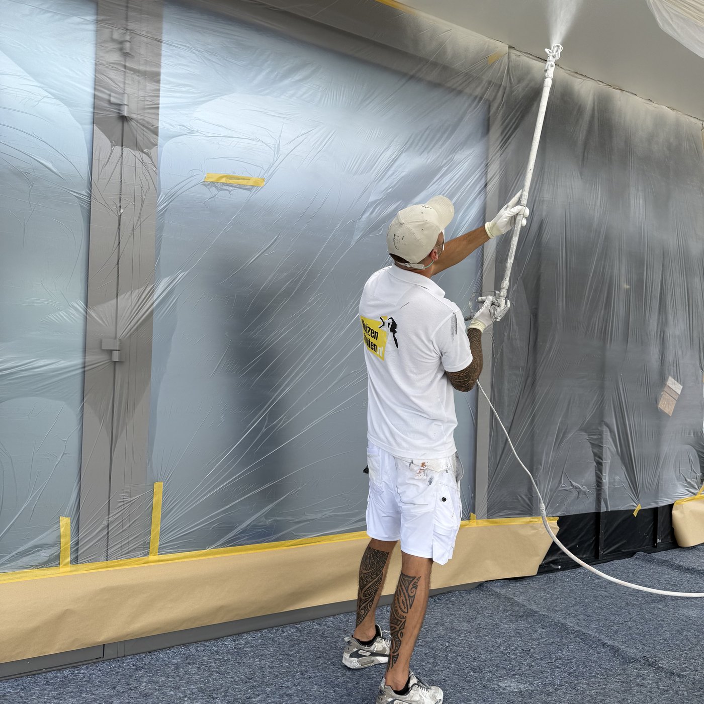 Vakman spuit een wand met airless latex, ruimte volledig afgeplakt met folie