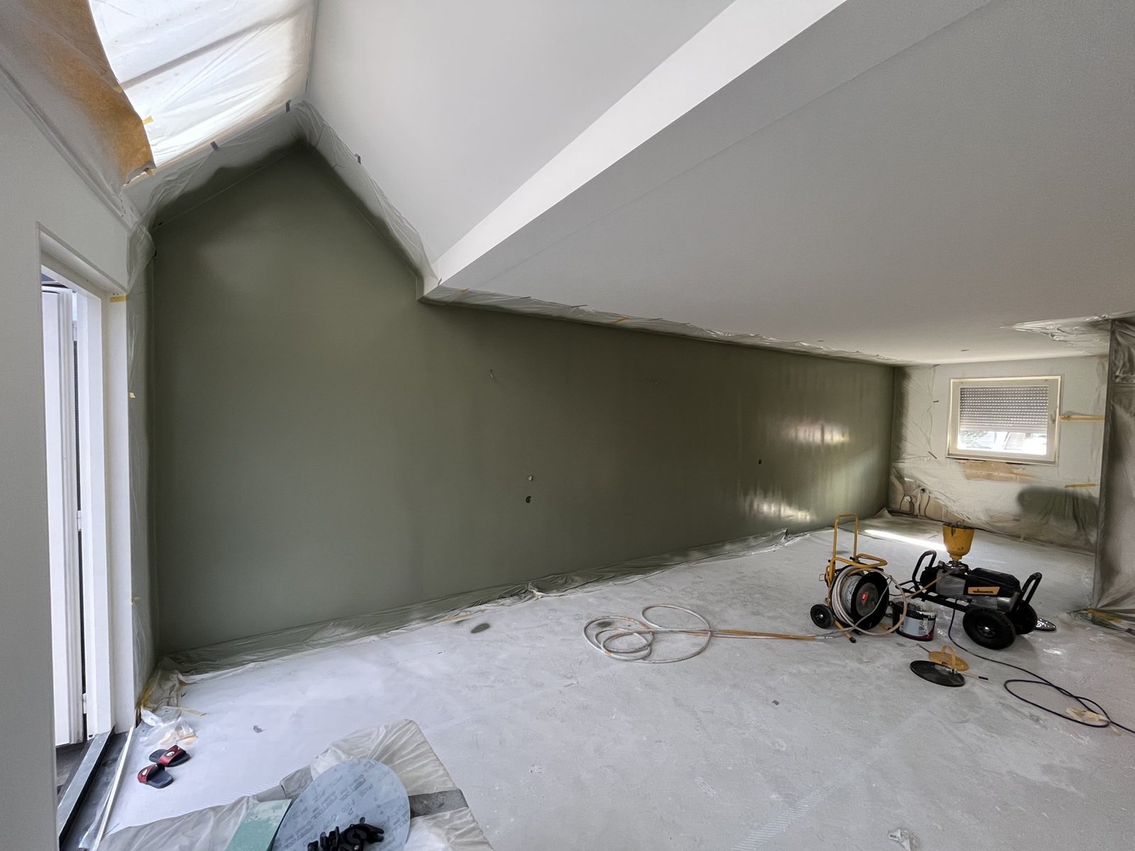 Zolderkamer met een groene wand en een strak gespoten wit plafond